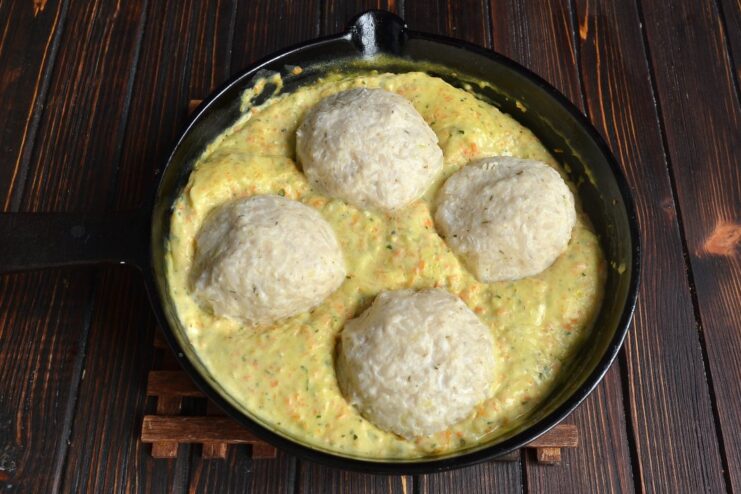 Steamed chicken meatballs being added to a skillet with simmering, creamy orange-colored vegetable gravy.