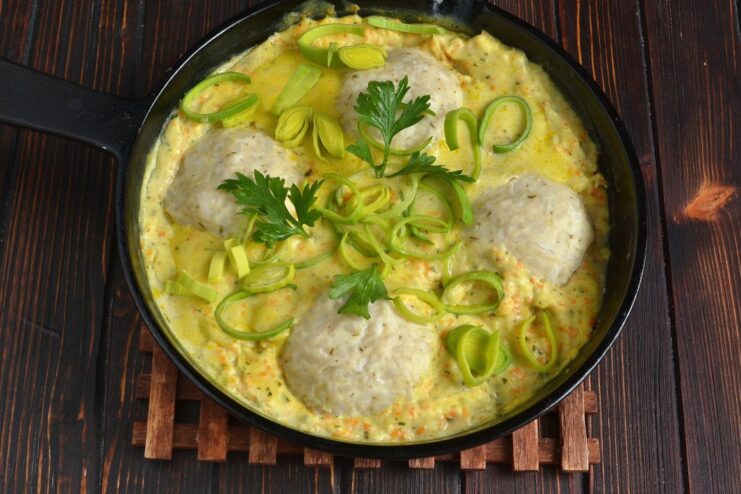 A close-up of the finished dish: steamed chicken meatballs in gravy in a pan, sprinkled with fresh green herbs.