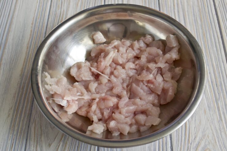 Close-up of chicken breast being minced on a cutting board to make fresh ground chicken.