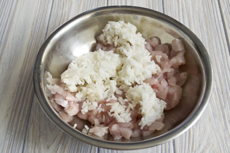 A bowl of ground chicken with cooked white rice being added to it.