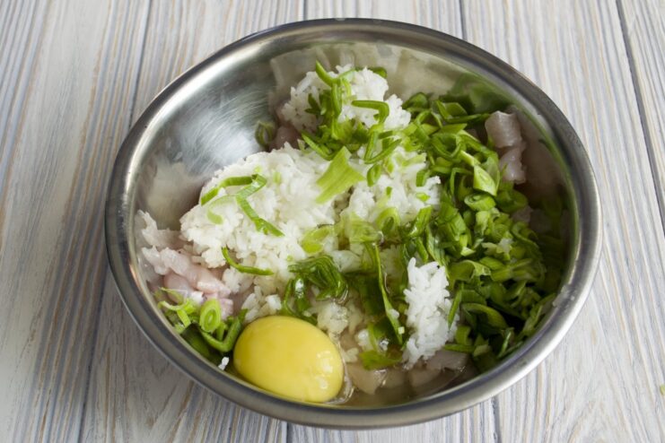 A raw chicken egg being cracked into the bowl with the ground meat mixture.