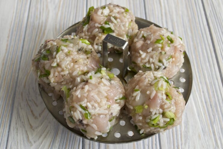Raw, formed tefteli meatballs placed in a steamer basket, ready for cooking.