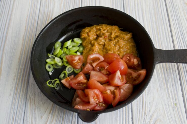 Chopped tomatoes, onions, and vegetable spread simmering in a skillet to create a sauce.