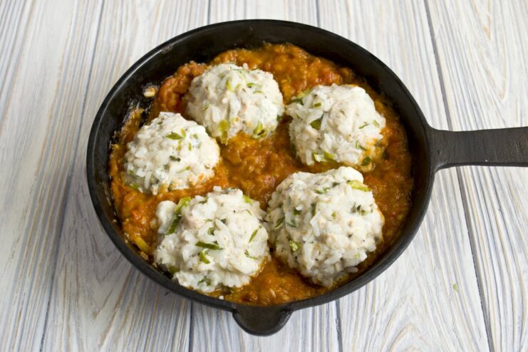 Cooked tefteli meatballs being gently simmered in a skillet with bubbling tomato sauce.