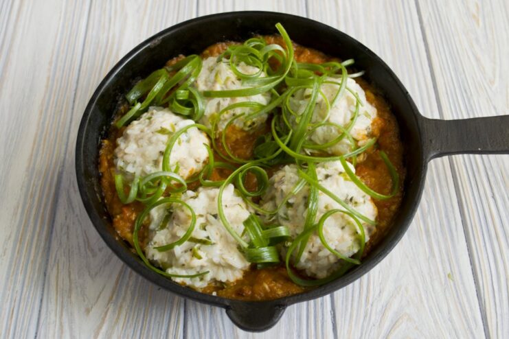 A final dish of tefteli in tomato sauce in a skillet, garnished with fresh chopped green onions.