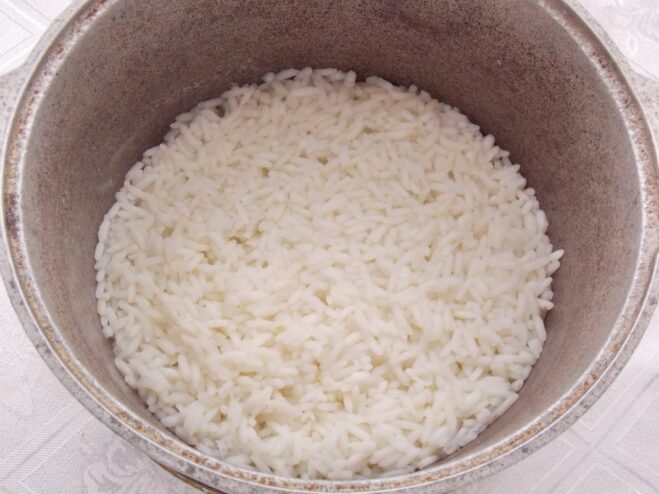 White rice cooking in a pot of water on the stove.