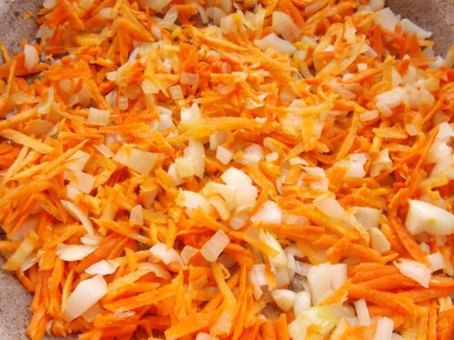 Finely chopped onion and grated carrot being sautéed in a frying pan.