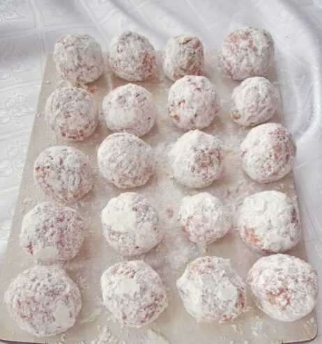 A raw meatball being rolled in a plate of white flour.