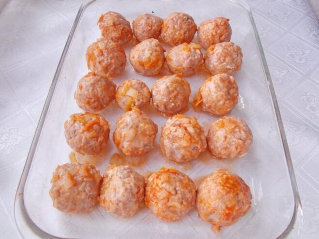 Raw meatballs arranged in neat rows in a glass baking dish.