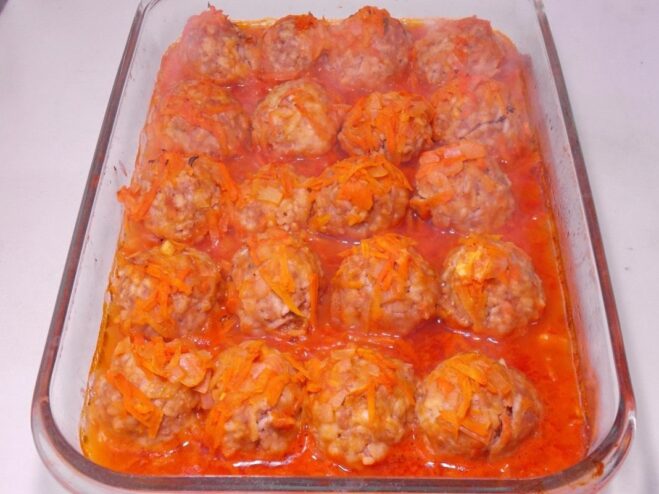 A baking dish with meatballs in tomato sauce baking in the oven.