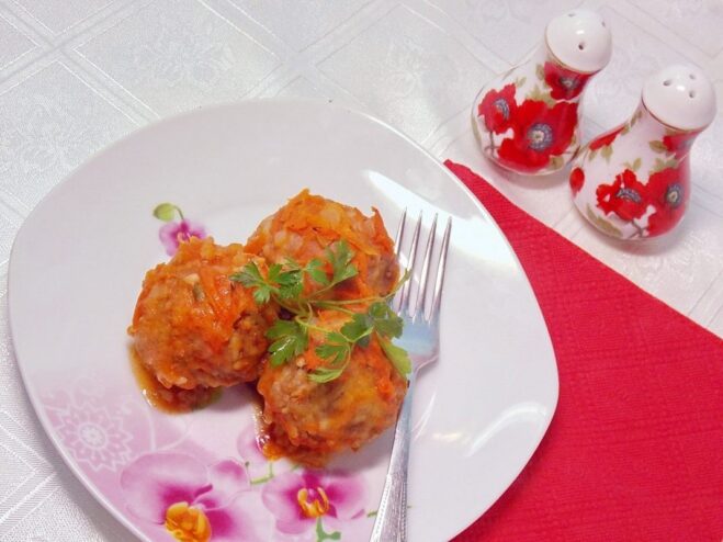 A plate of meatballs baked in tomato sauce, garnished with fresh herbs.