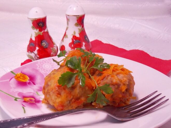 A plate of meatballs baked in tomato sauce, garnished with fresh herbs.