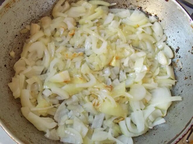 Sautéing chopped onions in a skillet until they become soft and translucent. Chopped onions being sautéed in a hot skillet with oil.