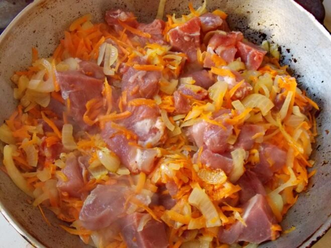 Searing the beef cubes with onions and carrots until browned. Cubes of beef being seared in a skillet with onions and carrots.