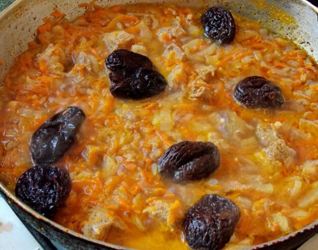Adding prunes to the beef stew for a touch of sweetness. Pitted prunes being added to the simmering beef stew in the skillet.