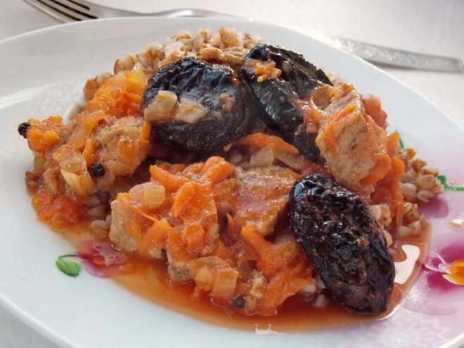 A plate of ready-to-eat braised beef with prunes, garnished with fresh herbs.