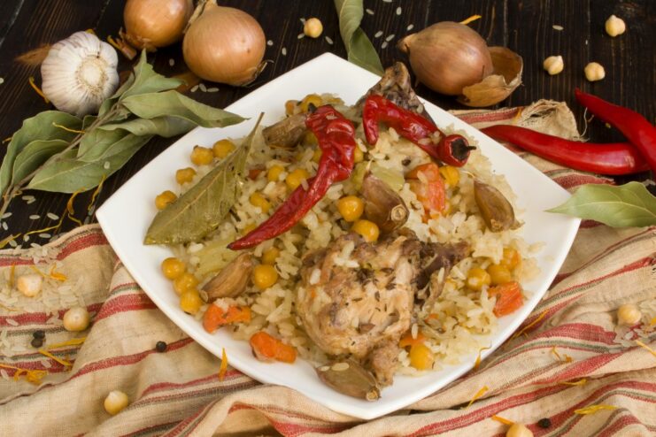 A large platter of freshly cooked Plov with chicken, chickpeas, and carrots, ready to be served.