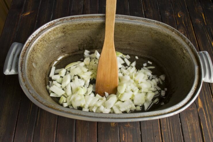 Frying onions until golden, the first step for a flavorful plov base Finely chopped onions being sautéed in hot oil in a large cast-iron Dutch oven.