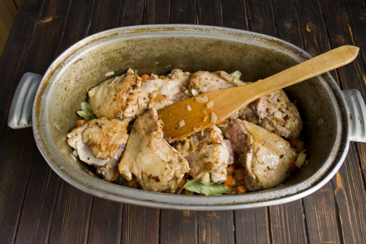Layering the seared chicken pieces over the vegetable base Golden-brown seared chicken thighs being placed on top of vegetables in the Dutch oven.