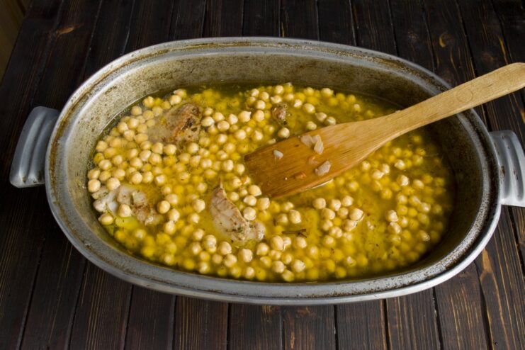 Adding a layer of soaked chickpeas to the plov Soaked chickpeas being added as a layer on top of the chicken in the Dutch oven.