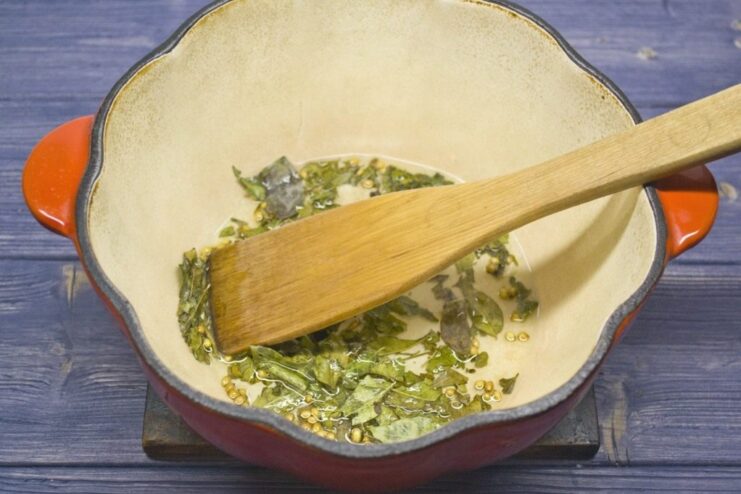 Toasting spices to release their aroma Dried curry leaves and coriander seeds sizzling in hot oil in a pot.