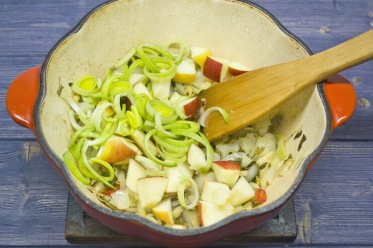Adding sweetness and flavor with leeks and apples Diced apples and sliced leeks being added to the sautéed vegetables in the pot.