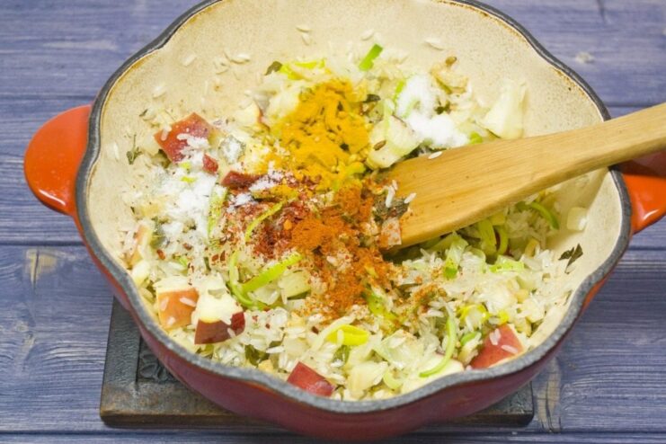 Toasting rice with spices before adding water Dry rice and spices being mixed with vegetables in a pot before adding water.