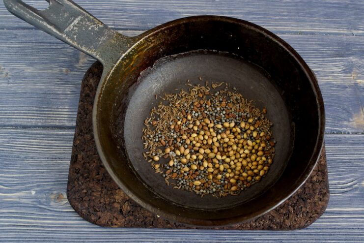 Toasting whole spices in a pan to release their aroma. A mix of cumin, mustard, and coriander seeds being toasted in a dry skillet.