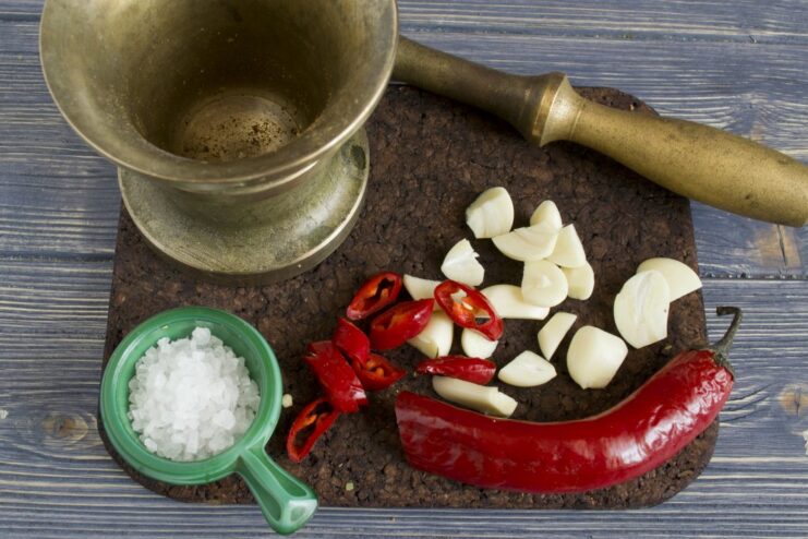 Creating an aromatic paste with salt, garlic, and chili. A mortar and pestle being used to crush sea salt, garlic, and chili into a paste.