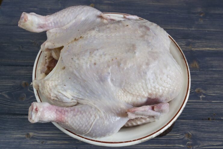 How to apply marinade under the chicken skin for maximum flavor. A hand carefully spreading marinade under the skin of a whole raw chicken.
