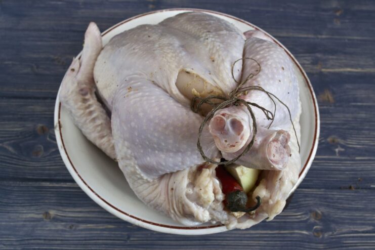 Stuffing the chicken cavity with aromatics before baking. A whole raw chicken being stuffed with quartered onion and a chili pepper.