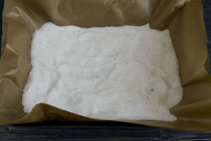 Preparing the salt bed for baking the chicken. A baking sheet lined with parchment paper, covered with a thick layer of coarse salt.