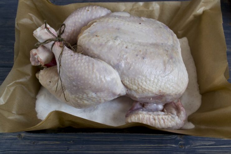 The chicken is ready for the oven, resting on its salt bed. A whole marinated chicken placed on a bed of salt, ready to go into the oven.