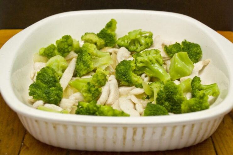 Adding Freshness: Combining Broccoli with Chicken Broccoli florets being added to the chicken strips in the baking dish.