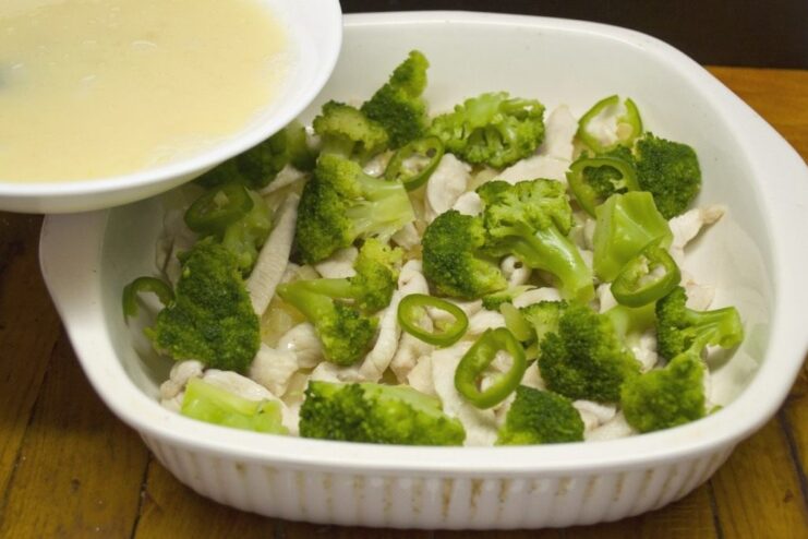 Adding a Kick: Seasoning with Green Chili Pepper Sliced green chili pepper being added to the broccoli and chicken in the baking dish.