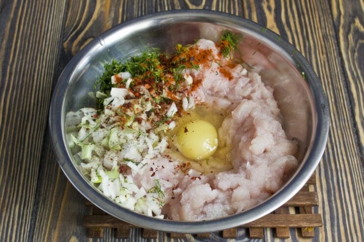 A bowl with ground meat, egg, chopped onion, and dill for making meatballs.