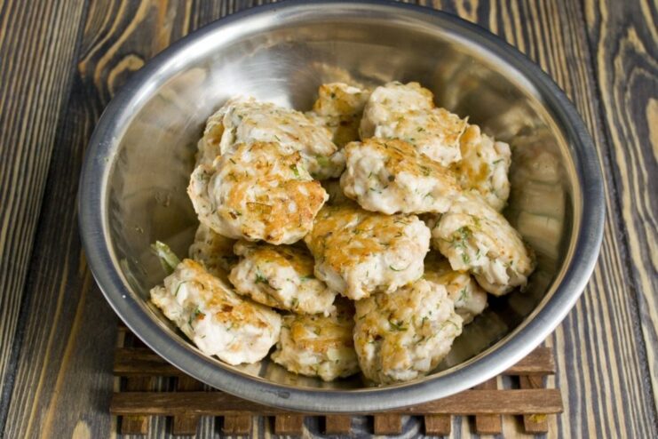 Golden-brown meatballs being fried in a non-stick skillet.