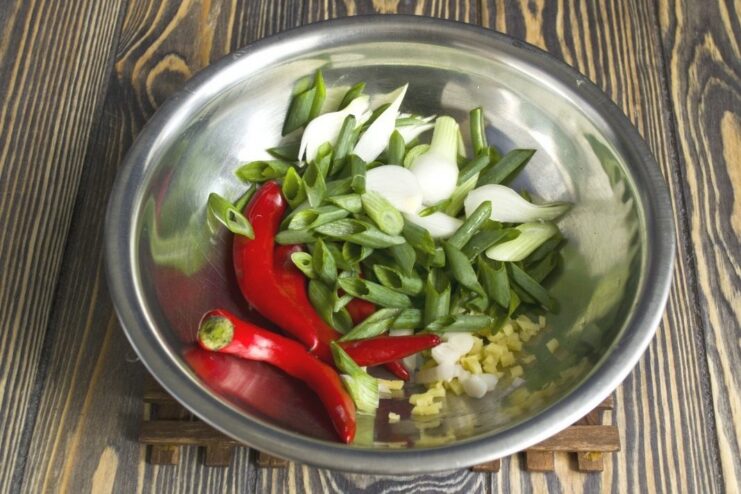 Chopped garlic, ginger, green onions, and whole chili peppers being sautéed in a pan.