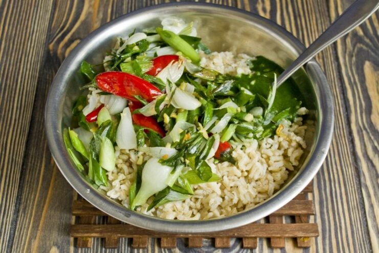 Cooked brown rice being mixed with green spinach puree and vegetables in a pot.