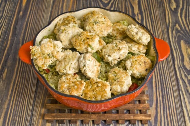 A braiser with green rice and meatballs being heated on the stove.