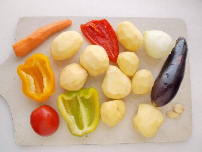 Preparing fresh vegetables for the fried potato dish A collection of fresh, washed vegetables like potatoes, carrots, and bell peppers on a cutting board.