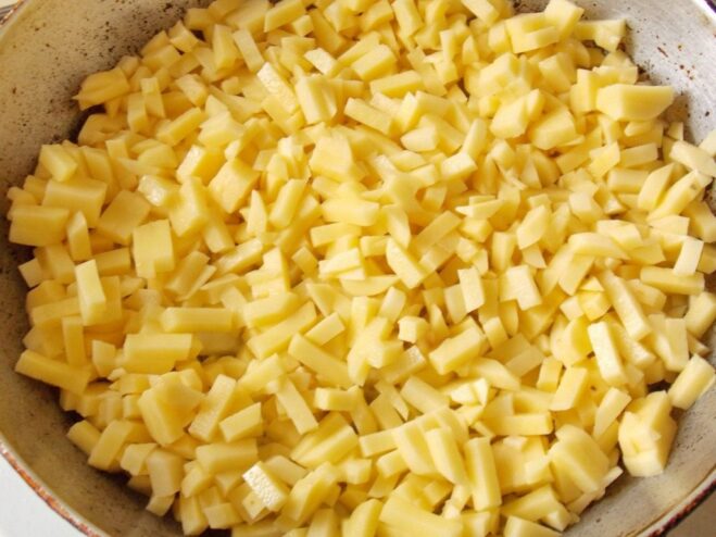 Slicing potatoes into strips for frying A person slicing potatoes into thin strips on a cutting board, with a pan in the background.