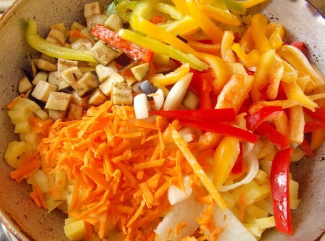 Combining vegetables with semi-cooked potatoes in the pan Chopped vegetables being added to a pan of half-fried potatoes.