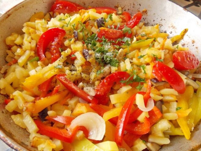 Final seasoning of the fried potatoes and vegetables Adding fresh tomatoes, herbs, and garlic to the skillet of fried potatoes and vegetables.