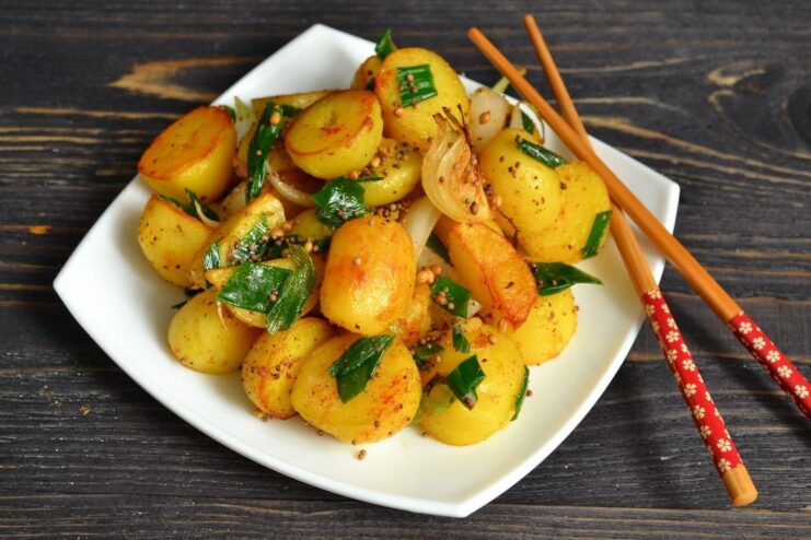Aromatic Indian-Style Spiced New Potatoes - A Perfect Side Dish A bowl of golden-brown Indian-style spiced new potatoes, garnished with green onions.