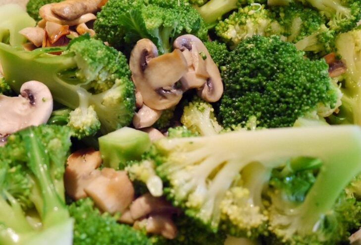 A plate of cooked broccoli with mushrooms, garnished with fresh herbs.