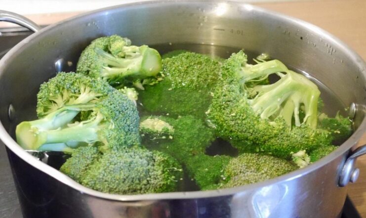 Blanching broccoli florets in a pot of boiling water to keep them crisp and green. Broccoli florets being cooked in a large pot of boiling water.