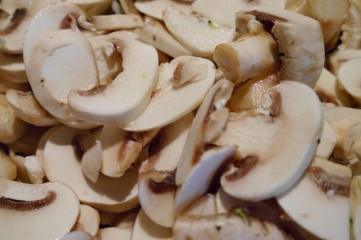 Sautéing sliced mushrooms in a pan until they are golden brown and flavorful. Sliced mushrooms being fried in a hot pan with oil.
