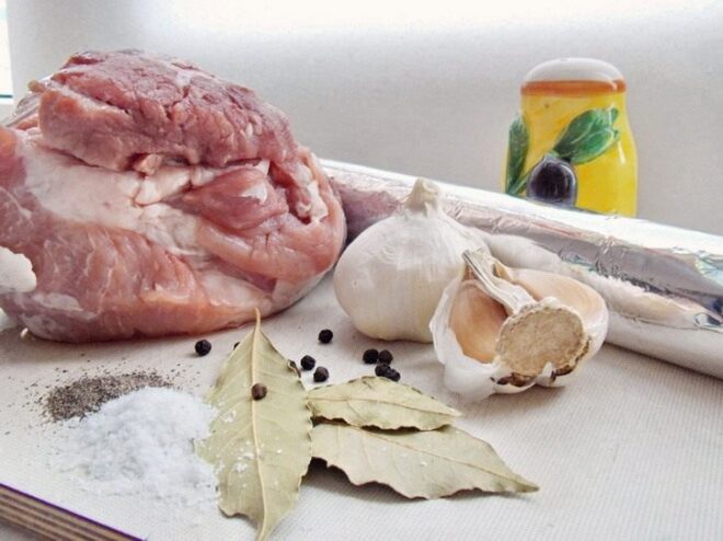 Essential Ingredients for Perfect Homemade Buzhenina Ingredients for homemade buzhenina: a piece of raw pork, garlic, bay leaves, and various peppercorns.