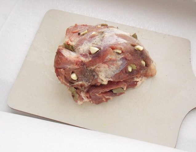 How to Stud Pork with Garlic and Spices for Maximum Flavor A hand studding a raw piece of pork with garlic cloves and spices before roasting.